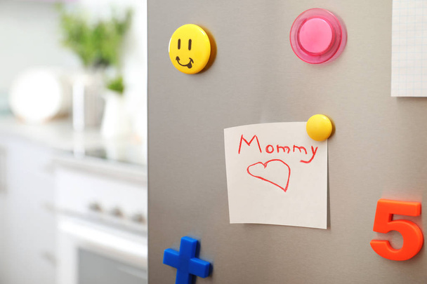 Note with word "Mommy" and colorful magnets on refrigerator door in kitchen. Space for text - Foto, afbeelding