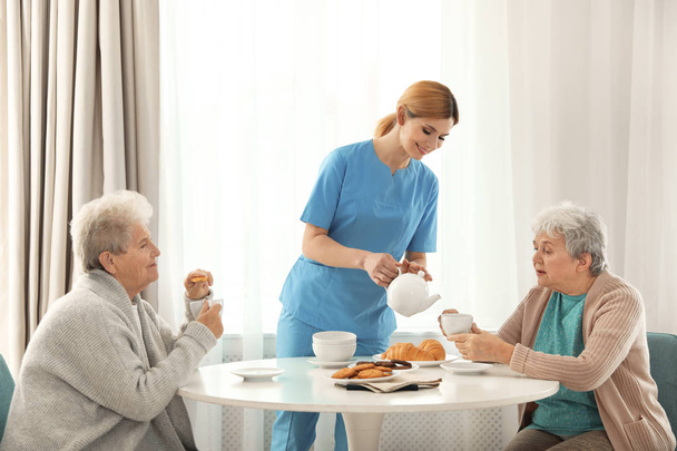 Nurse assisting while elderly women having breakfast at retirement home - Photo, image