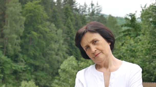 Retrato feminino de insatisfeito chateado mulher mais velha com cabelo escuro curto e rosto enrugado olhando para a câmera com desaprovação ao ar livre na colina da montanha com floresta verde no fundo
 - Filmagem, Vídeo