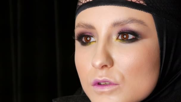 Profesionální dívčí model s nádherným make-upem představuje v černé čepici na hlavě před kamerou na černém pozadí v obraze černé vdovy. High-móda - Záběry, video