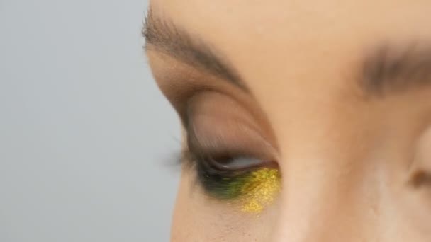 Fashionable multi-colored eye shadow chameleon with yellow purple gray silver color on the eyelid of beautiful girl model with brown eyes. Professional cosmetic makeup. Eye close up view - Footage, Video