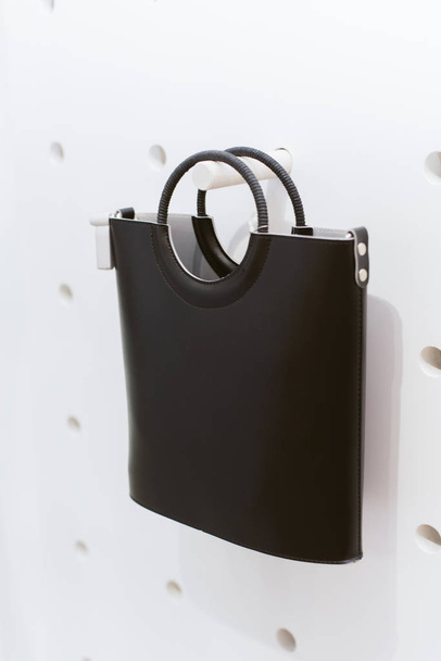 Μαύρη κλασική δερμάτινη τσάντα με στρογγυλές λαβές σε ένα ράφι σε ένα κατάστημα. Κομψή περιστασιακή γυναικεία τσάντα - Φωτογραφία, εικόνα