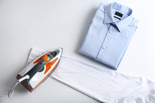 Iron with clean shirts on light background, top view - Φωτογραφία, εικόνα