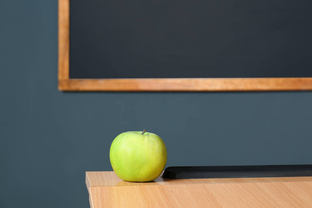 Wooden school desk and apple near blackboard on grey wall - Foto, imagen