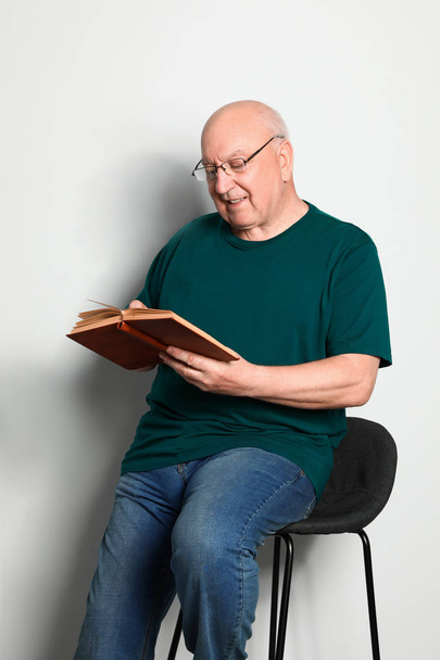 Portrait of senior man with glasses reading book on light background - Foto, afbeelding