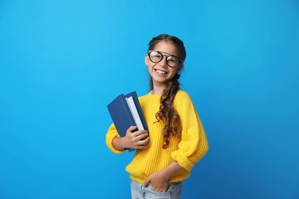 Cute little girl with glasses and books on blue background. Reading concept - Zdjęcie, obraz