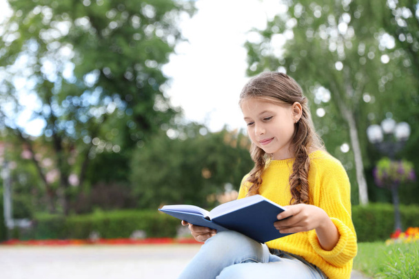 Cute little girl reading book in green park - Foto, Imagen