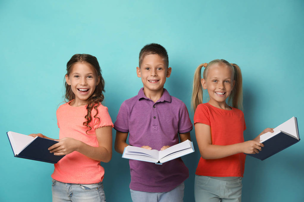 Portrait of little children reading books on turquoise background - 写真・画像