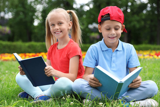 Χαριτωμένα μικρά παιδιά που διαβάζουν βιβλία για το πράσινο γρασίδι στο πάρκο - Φωτογραφία, εικόνα