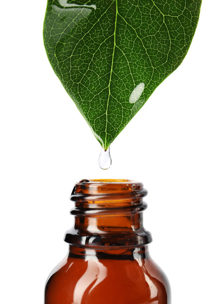 Essential oil drop falling from green leaf into glass bottle on white background, closeup - Foto, Imagen