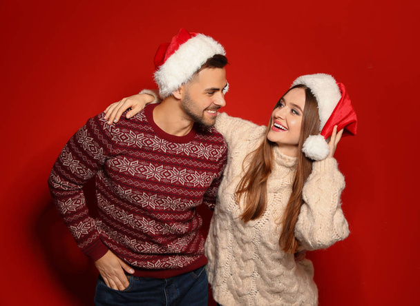 Couple wearing Christmas sweaters and Santa hats on red background - Foto, immagini