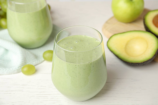 Glass of tasty avocado smoothie and ingredients on white wooden table - Фото, изображение