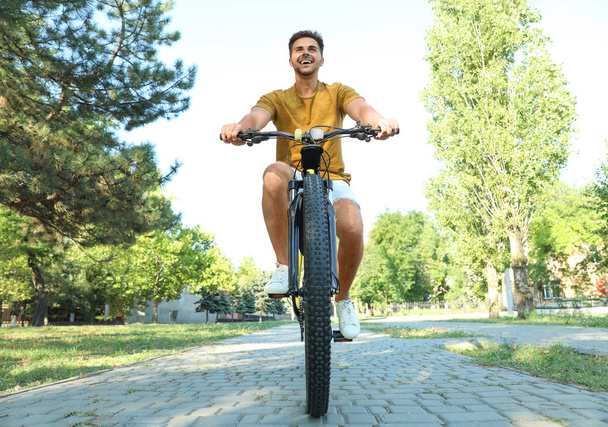 Handsome young man with bicycle in city park, low angle view - Φωτογραφία, εικόνα
