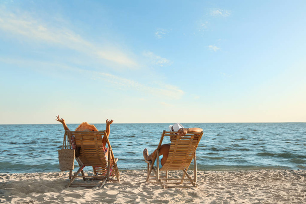 Young couple relaxing in deck chairs on beach near sea - Photo, image