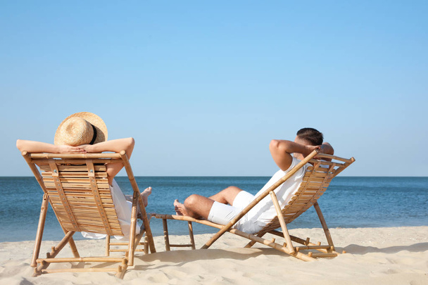 Young couple relaxing in deck chairs on beach - Photo, image