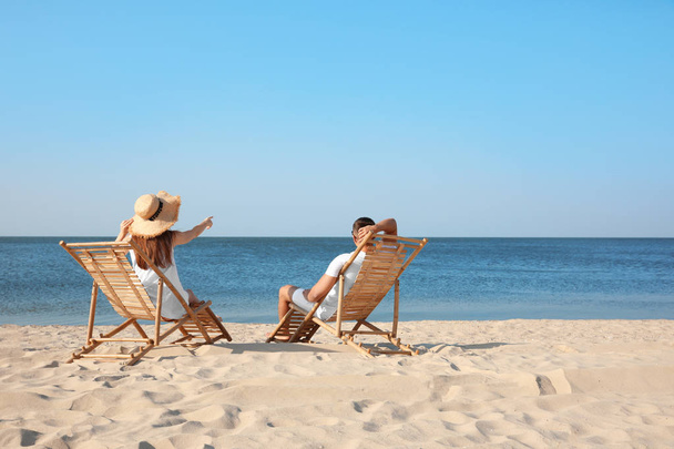 Young couple relaxing in deck chairs on beach - Фото, изображение