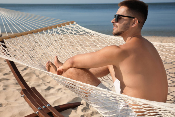 Young man relaxing in hammock on beach - Фото, изображение