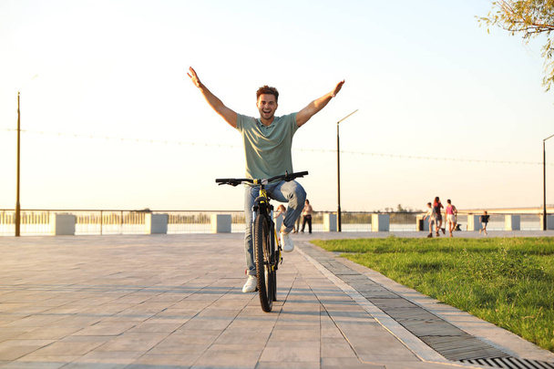 Handsome young man riding bicycle on city waterfront - Photo, image
