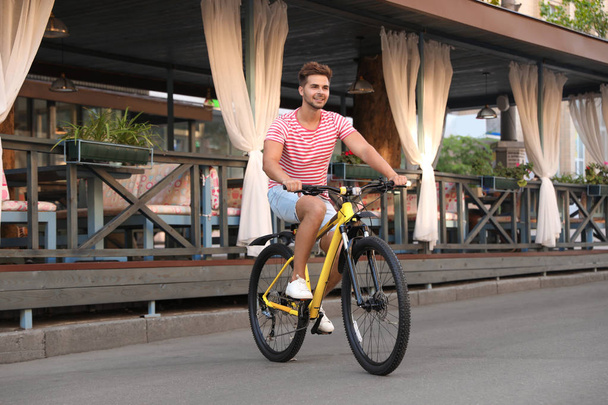 Handsome young man riding bicycle on city street - Fotó, kép