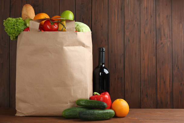 Shopping paper bag with different groceries on table against wooden background. Space for text - Фото, зображення