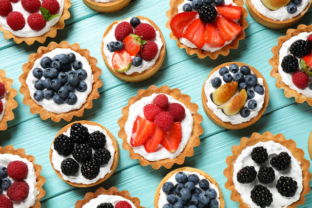 Many different berry tarts on blue wooden table, flat lay. Delicious pastries - Foto, imagen