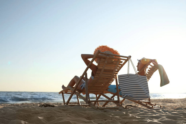Молода пара розслабляється в стільцях палуби на пляжі біля моря
 - Фото, зображення