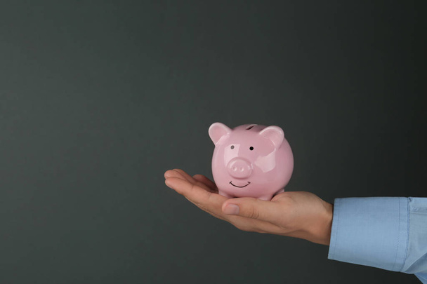 Man holding piggy bank on dark grey background, closeup view. Space for text - Foto, Imagen