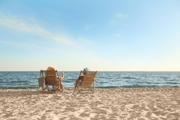 Young couple relaxing in deck chairs on beach near sea - Φωτογραφία, εικόνα