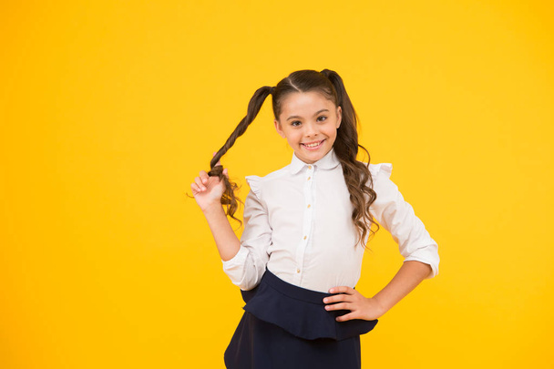Her twisted hairdo. Small girl winding long hairdoaround her finger on yellow background. Little kid with ponytail hairdo in school uniform. Child with new hairdo for back to school - Zdjęcie, obraz