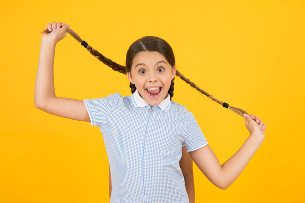 small girl in school uniform. retro look. child hold pigtail of girl behind. old school. kid fashion. happy child on yellow background. vintage fashion beauty. childhood happiness. what a surprise - Foto, afbeelding