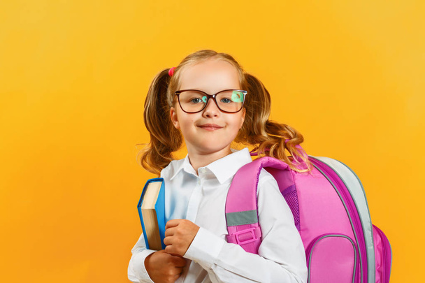 Porträt eines kleinen Mädchens mit Rucksack und Buch auf gelbem Hintergrund. charmante Kinderstudentin Nahaufnahme. zurück zur Schule. das Konzept der Bildung - Foto, Bild