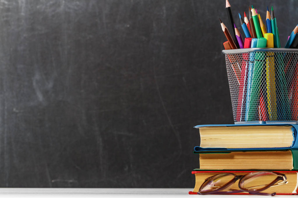 Куча книг, очков, карандашей на фоне черной школьной доски. Концепция образования. Копирование пространства
 - Фото, изображение