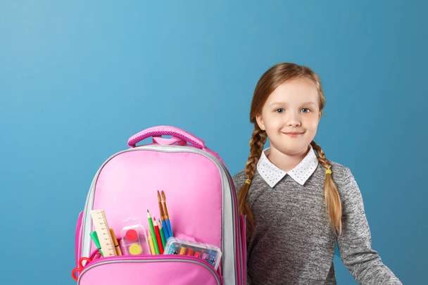 Closeup portrait of little girl schoolgirl with backpack on blue background. Back to school. The concept of education. - Фото, зображення