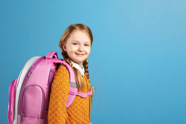 Portrait of a little girl schoolgirl with a backpack on a blue background. Back to school. The concept of education. - Foto, Imagem