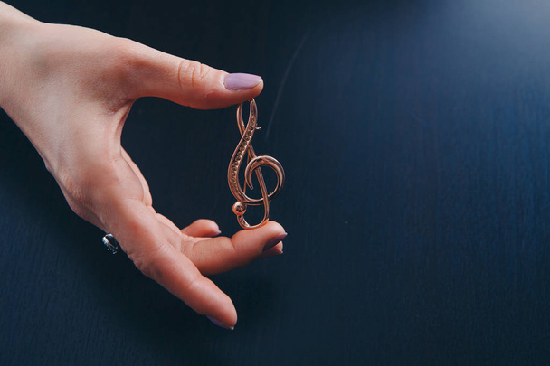 Golden violin key in the hands of women. jewellery: brooch and rings. copy space - Fotó, kép