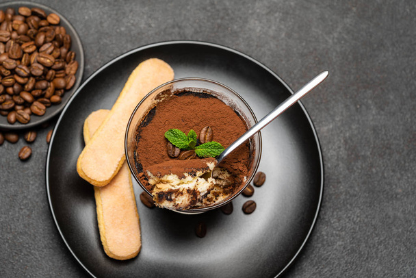 Portion of Classic tiramisu dessert in a glass cup on dark concrete background - Zdjęcie, obraz