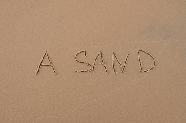 The inscription "Sand" painted on the sand. Sand background with a pattern. Summer. Day. Sea shore. - Photo, Image