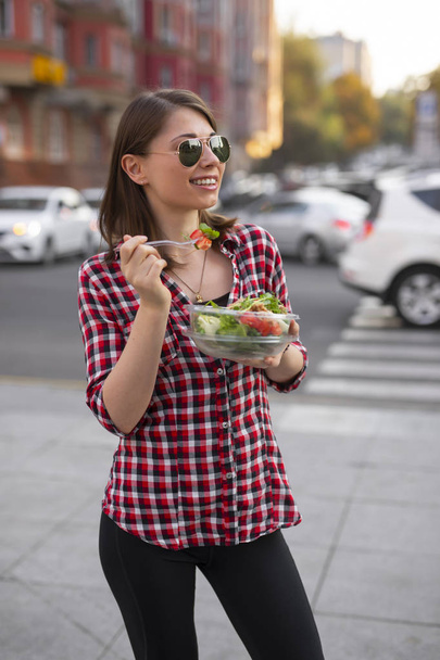 Jonge vrouw die salade eet bij Urban City outdoor, diner snack - Foto, afbeelding