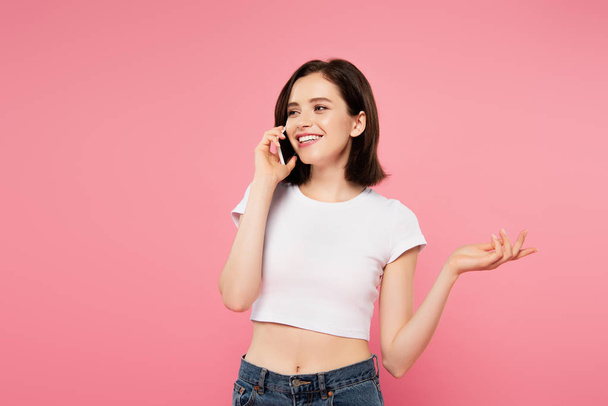 beautiful smiling girl talking on smartphone and gesturing isolated on pink - Valokuva, kuva