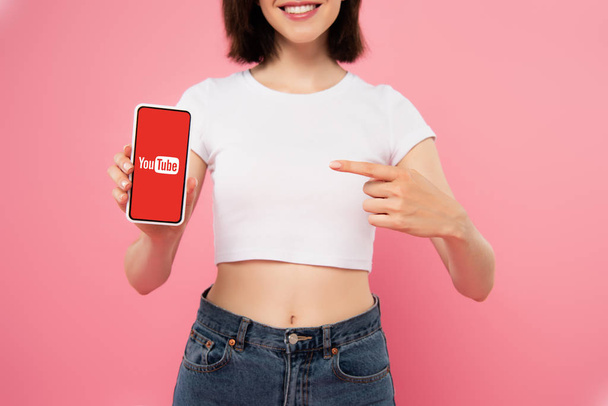 Київ, Україна-3 липня 2019: обрізаний вигляд дівчини вказуючи пальцем на смартфон з логотипом YouTube, ізольованих на рожевому - Фото, зображення