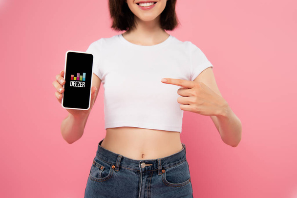 KYIV, UKRAINE - JULY 3, 2019: cropped view of girl pointing with finger at smartphone with deezer logo isolated on pink - Foto, immagini