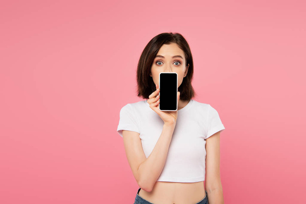 surprised girl holding smartphone with blank screen isolated on pink - 写真・画像