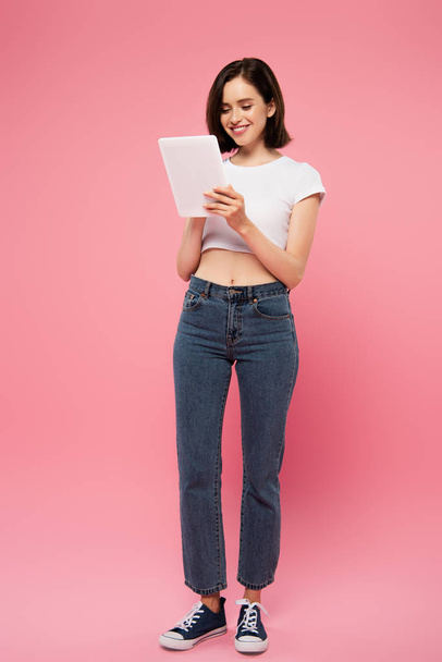 full length view of beautiful smiling girl using digital tablet isolated on pink - Φωτογραφία, εικόνα