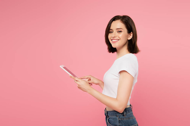 Widok z boku pięknej uśmiechniętej dziewczyny za pomocą cyfrowego tabletu na różowo - Zdjęcie, obraz