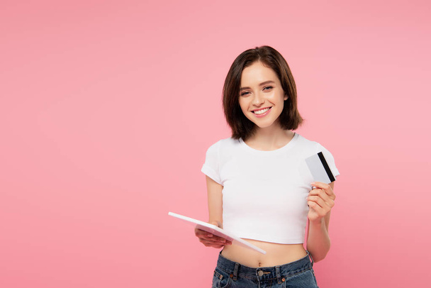 chica sonriente sosteniendo tableta digital y tarjeta de crédito aislada en rosa
 - Foto, Imagen