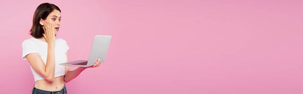 tiro panorâmico de menina bonita chocada usando laptop isolado em rosa
 - Foto, Imagem