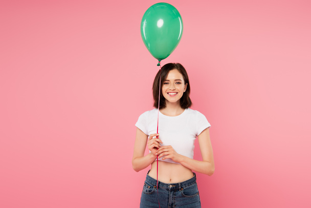 χαμογελαστή όμορφη κοπέλα κρατώντας πράσινο μπαλόνι απομονωθεί σε ροζ - Φωτογραφία, εικόνα