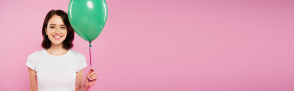 панорамный снимок улыбающейся красивой девушки, держащей зеленый шар, изолированный на розовый
 - Фото, изображение