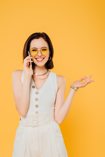 mosolygós elegáns nő napszemüveg beszél okostelefon izolált sárga - Fotó, kép