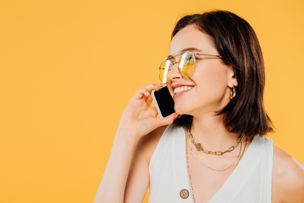 黄色で孤立したスマートフォンで話すサングラスで笑顔のエレガントな女性 - 写真・画像